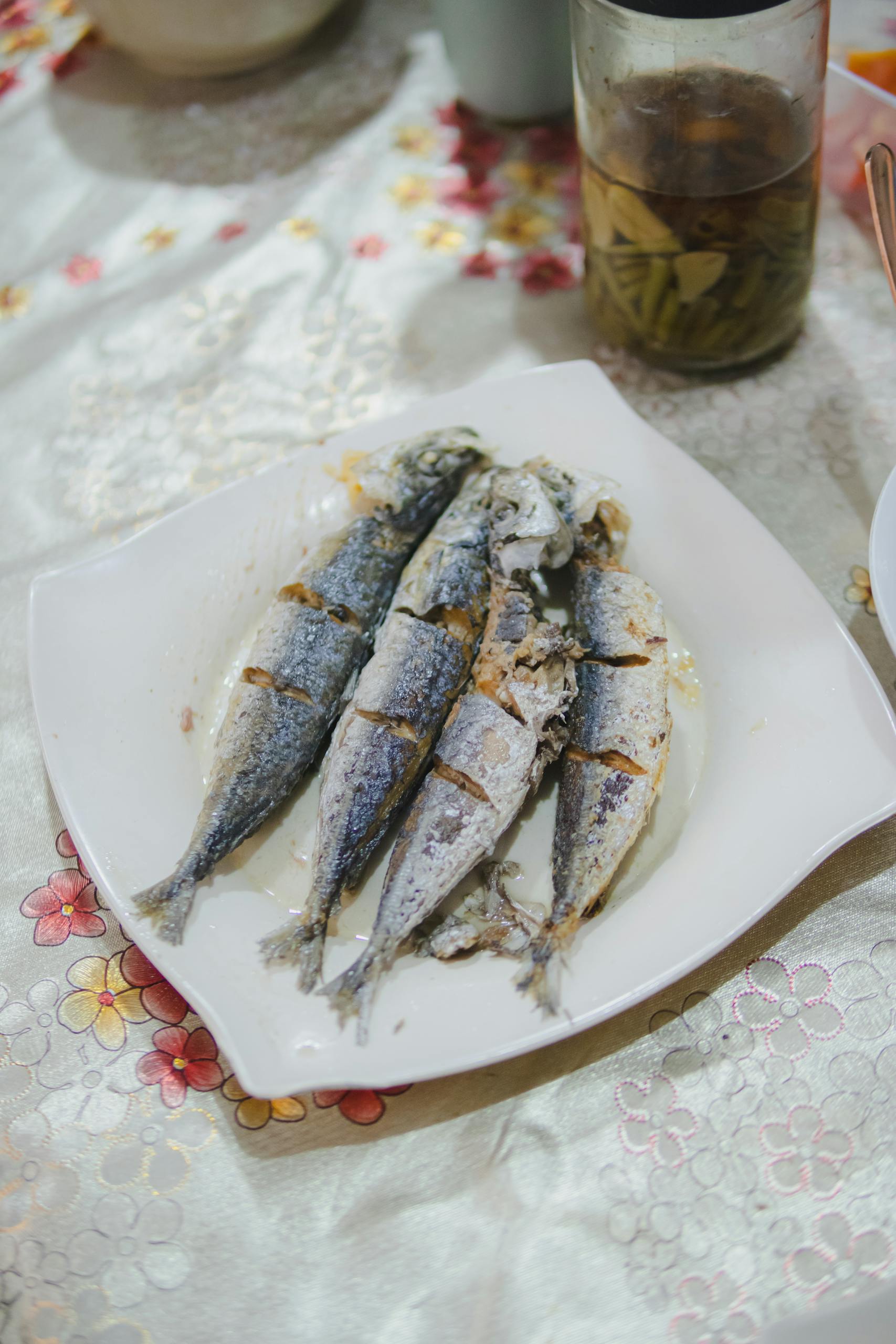 Four fried fish served on a white plate with floral tablecloth. Perfect for food lovers.